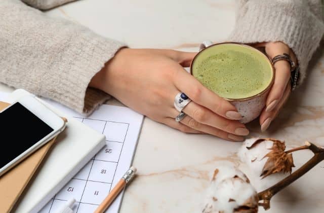 温かい抹茶ラテが注がれた陶器のカップを両手で持つ女性、器の質感と温もりで五感を深める食体験