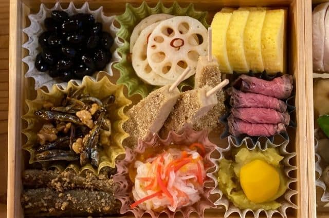 オモテワシケースを使って重箱に美しく盛り付けられた伝統的なおせち料理、様々なおかずを彩る