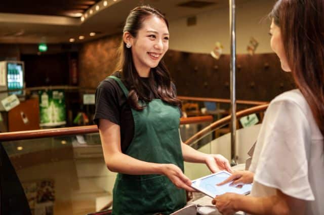 リユース型エコ容器をお客様に勧める笑顔の女性店員、顧客エンゲージメント向上